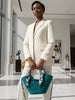 Woman in a white suit holding a teal handbag in a modern indoor setting