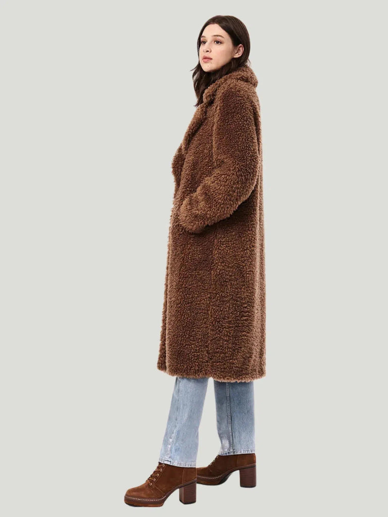 Teddy Embrace Vegan Fur Coat by Bernardo, oversized and below knee-length, in luxurious teddy texture. Made with 100% polyester faux fur and lined with 100% recycled polyester, it features eco-friendly Ecoplume™ insulation for extra warmth. Model is 5’10” and wears size S. Dry clean only. This coat combines style with sustainability, using insulation from 100% post-consumer recycled plastic bottles."