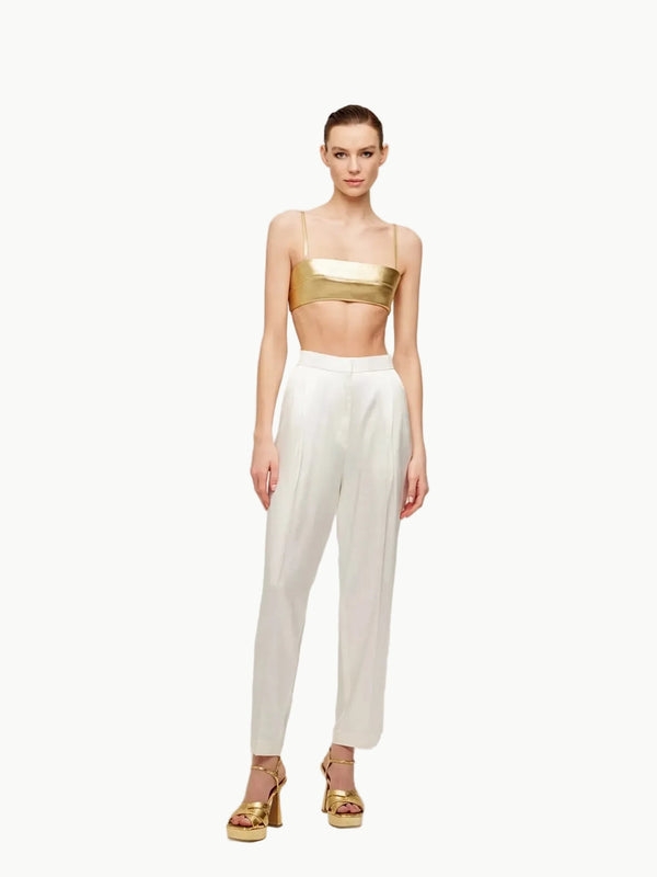Model wearing a gold top and white pants on a plain background