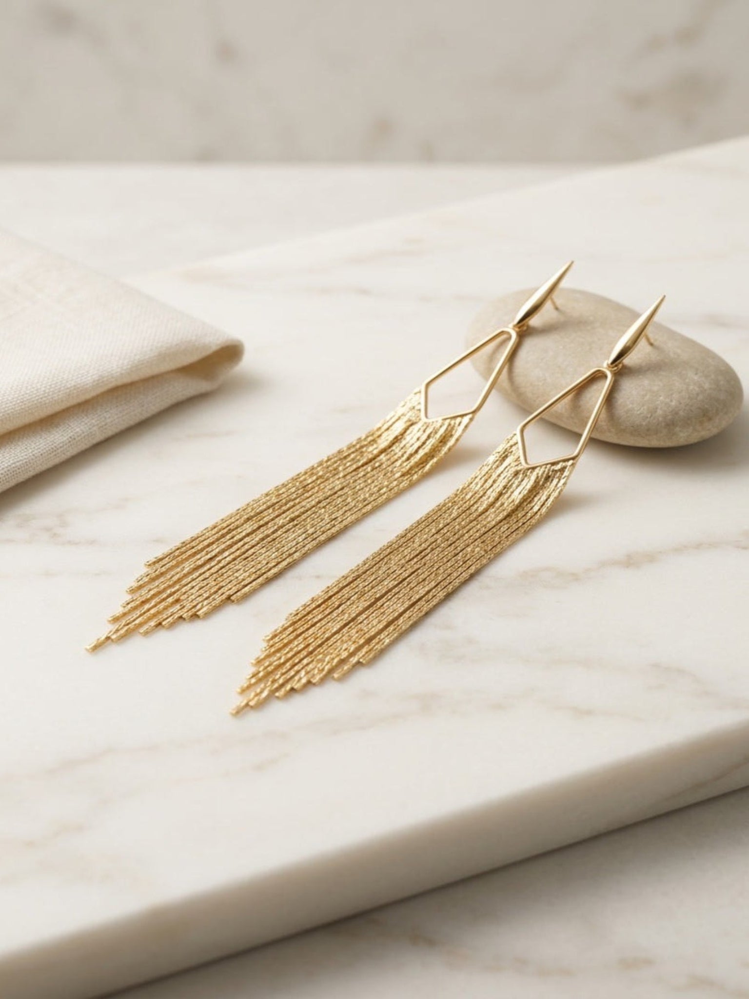 Gold tassel earrings on a marble surface