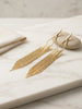 Gold tassel earrings on a marble surface