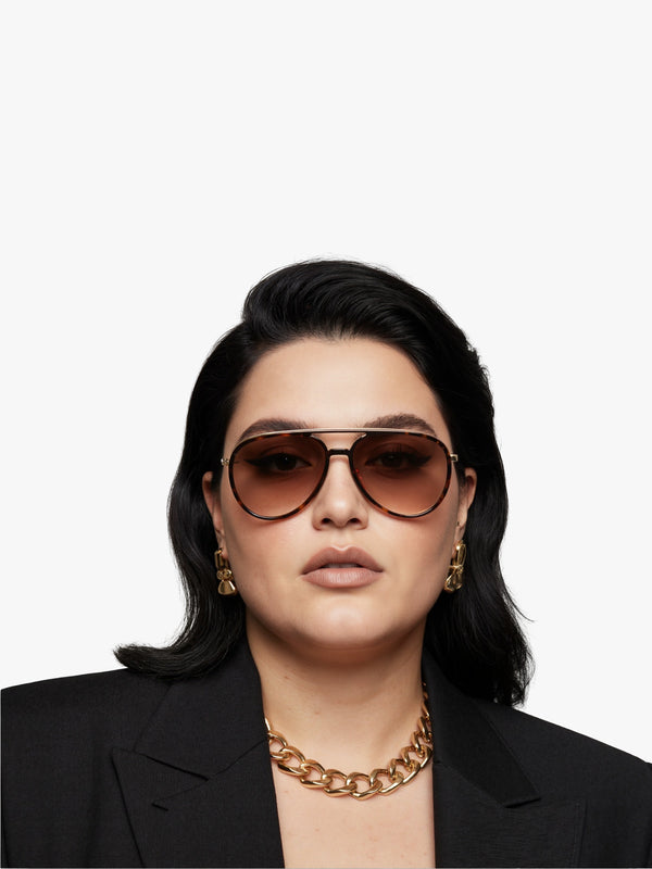Person wearing sunglasses and a black blazer with a gold chain necklace on a white background