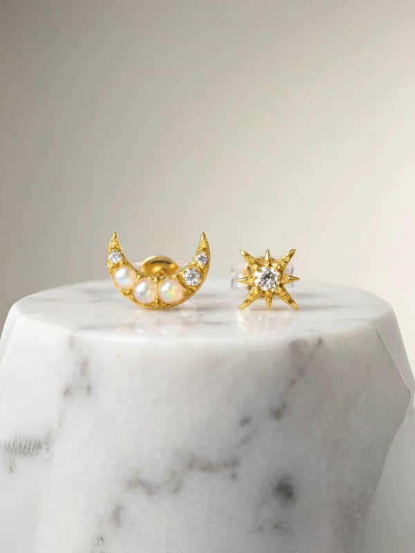 Gold earrings shaped like a moon and a star on a marble surface
