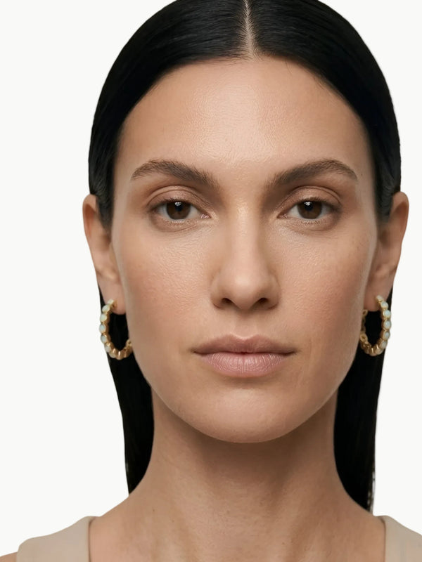 Woman wearing gold hoop earrings with a plain background