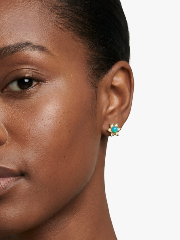 Close-up of a woman wearing a gold earring with a turquoise stone on a white background