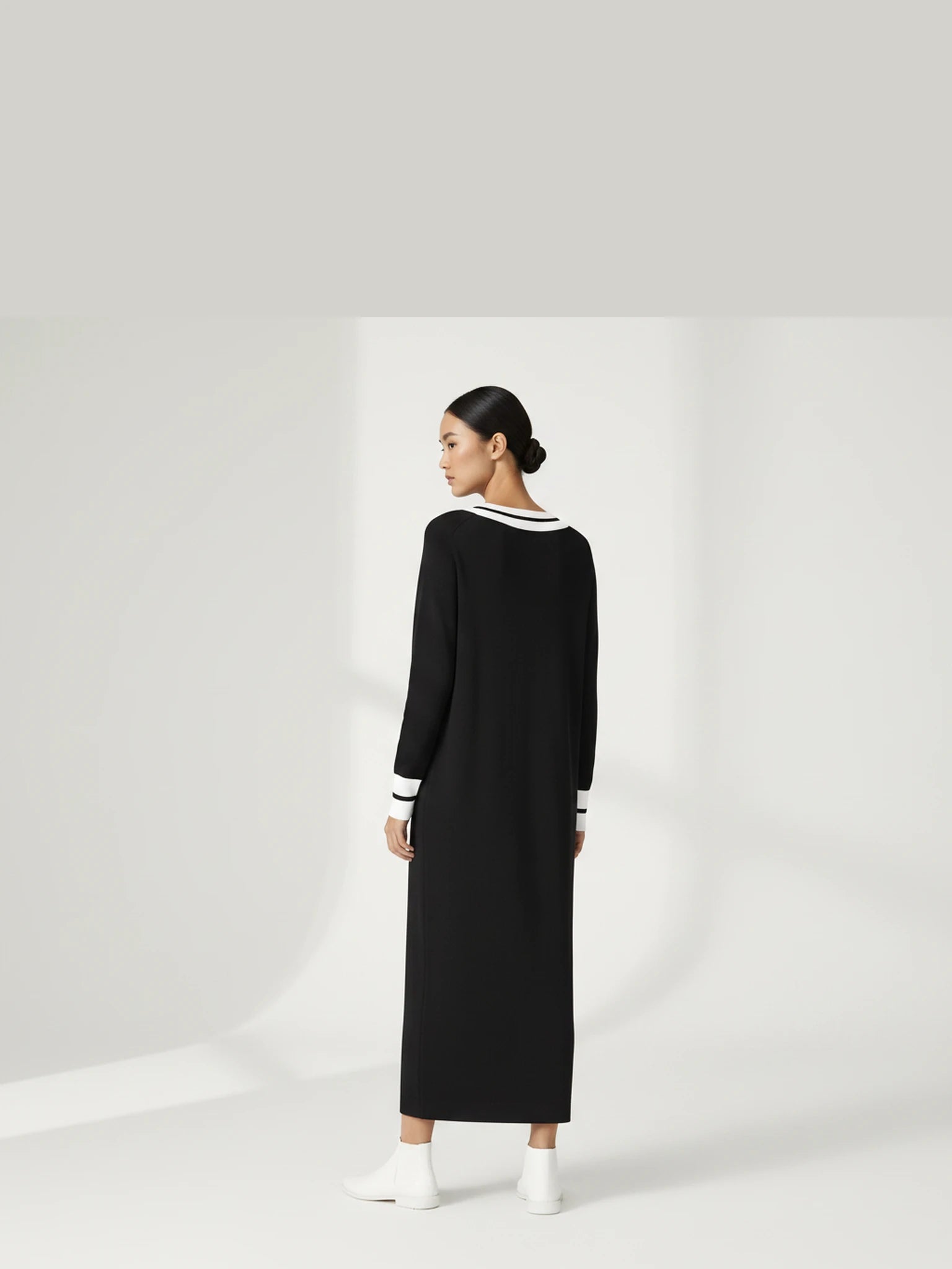 Detail back-facing view of the model walking in the Lanhtropy Preppy Knitted Dress in black, paired with white boots to showcase styling and movement.