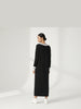 Detail back-facing view of the model walking in the Lanhtropy Preppy Knitted Dress in black, paired with white boots to showcase styling and movement.