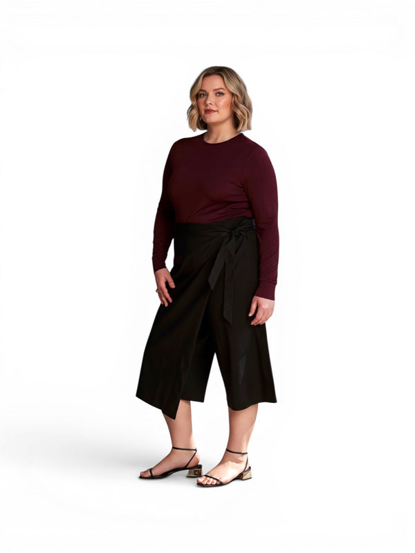 Queen Anna House of Fashion model wearing black linen wrap culottes with a burgundy long-sleeve top and black sandals.