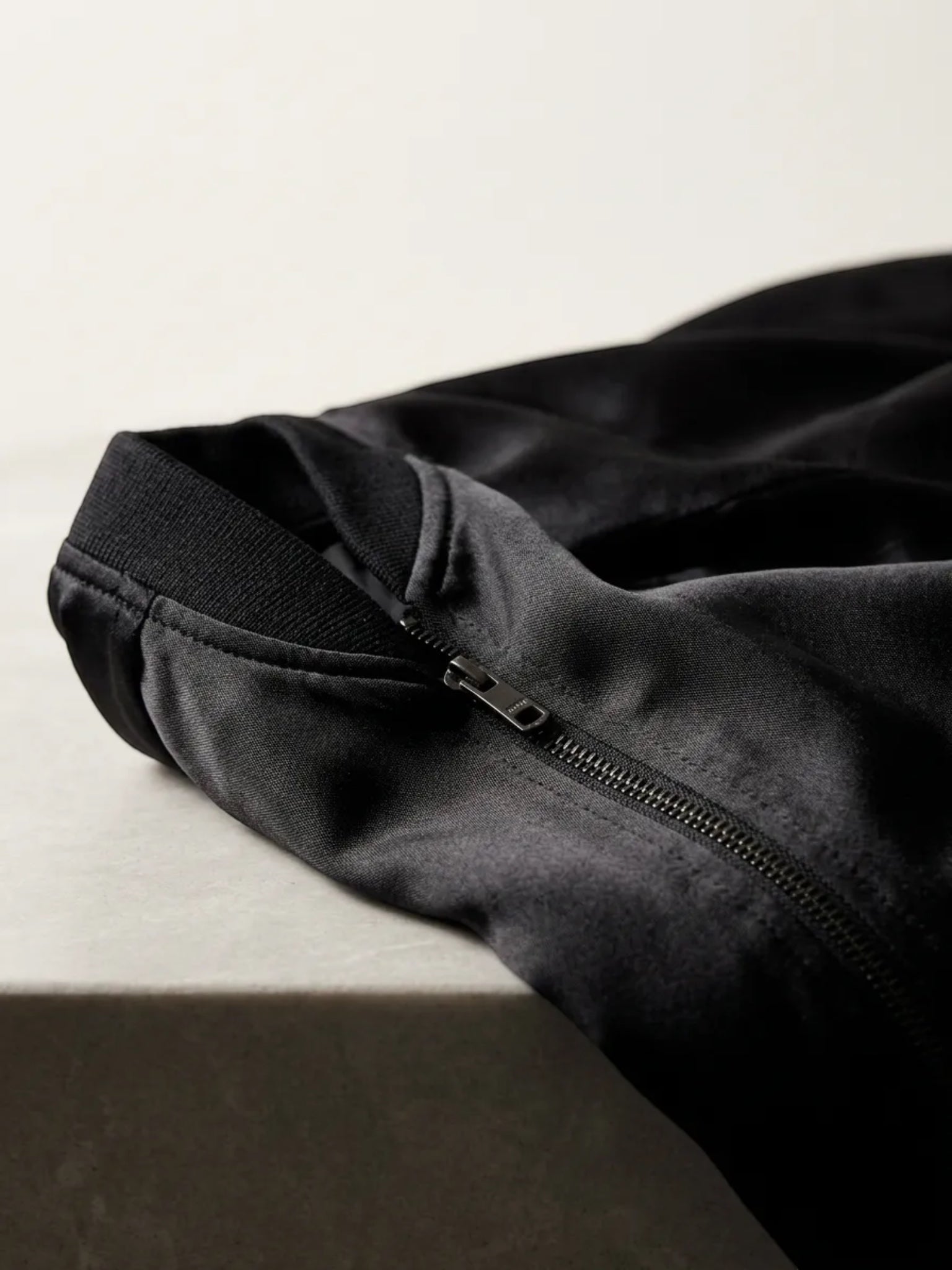Queen Anna House of Fashion black satin bomber jacket featuring tonal ribbed collar and zip closure detail.