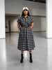 Queen Anna House of Fashion model wearing a black and white plaid midi shirtdress with a brown belt and white cap.