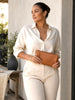 Queen Anna House of Fashion TAH Bags minimalist tan leather clutch held by a woman in a cream linen outfit.