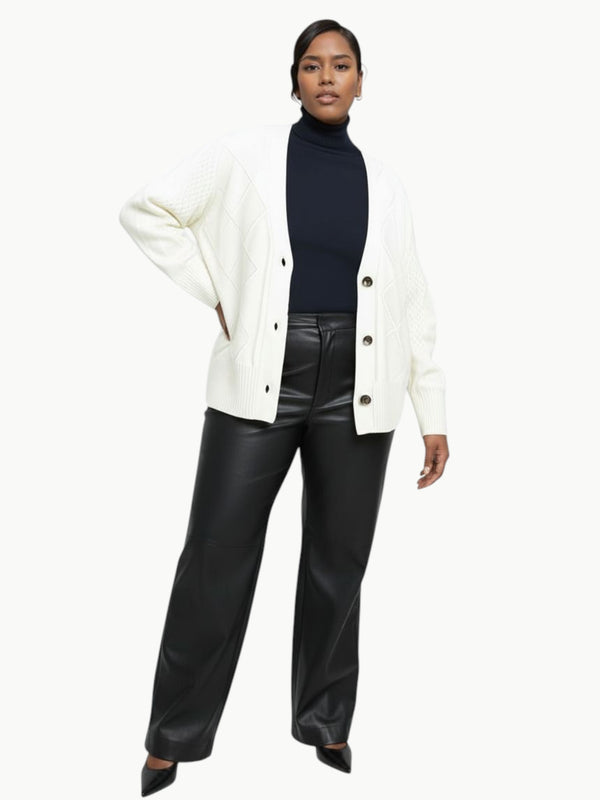 Model wearing a Queen Anna House of Fashion white cable knit cardigan over a black turtleneck and leather trousers.