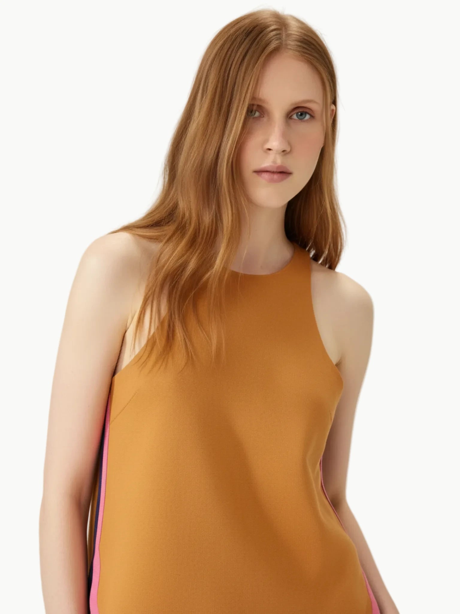 Woman wearing a mustard yellow sleeveless top against a plain background